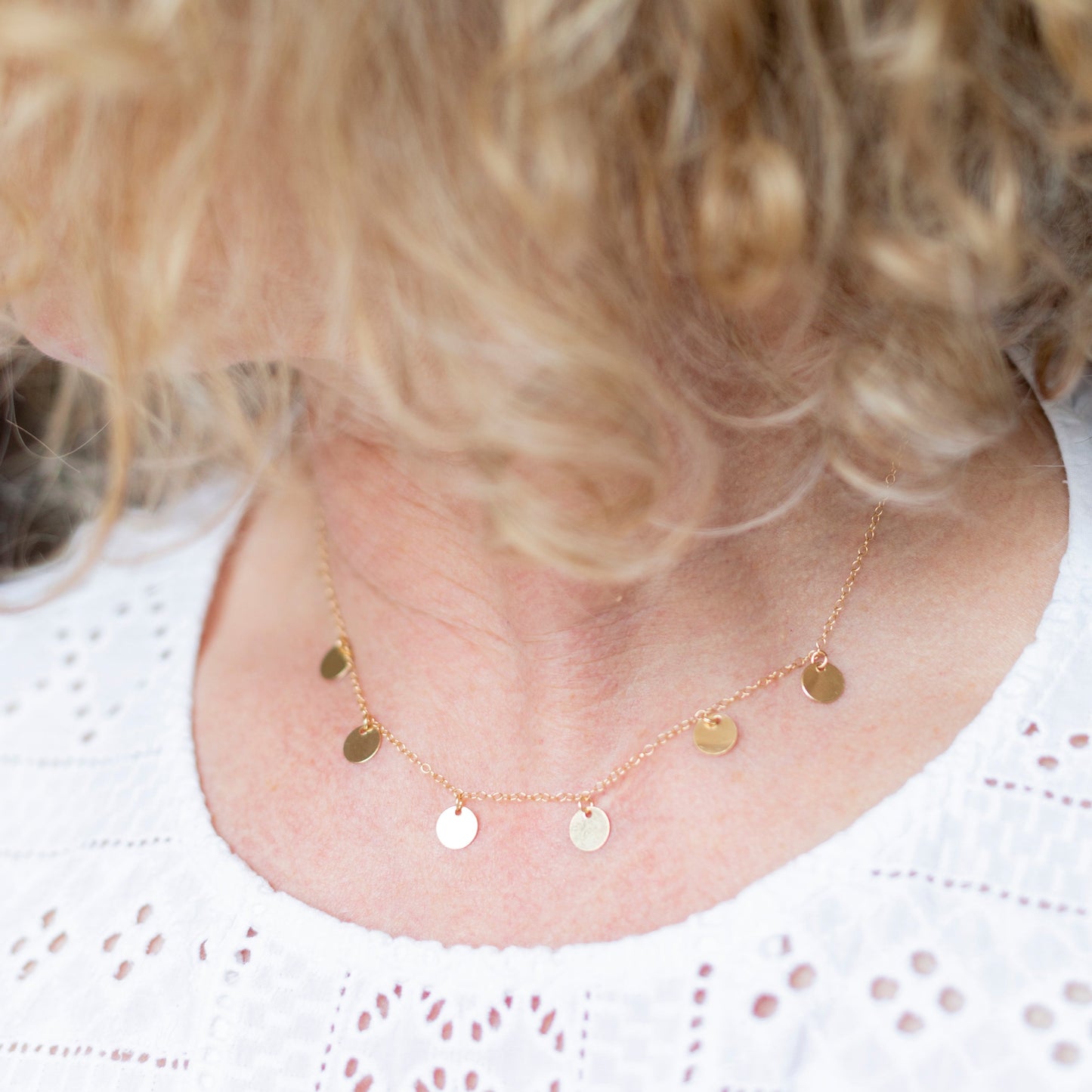 Necklace with small round pendants worn by a person with blonde hair.