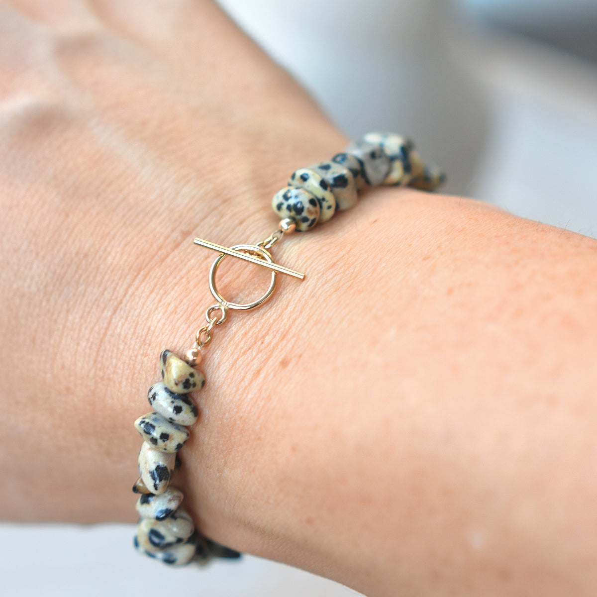 A close-up of a person's wrist wearing a beaded bracelet with black and white marbled beads and a gold toggle clasp.