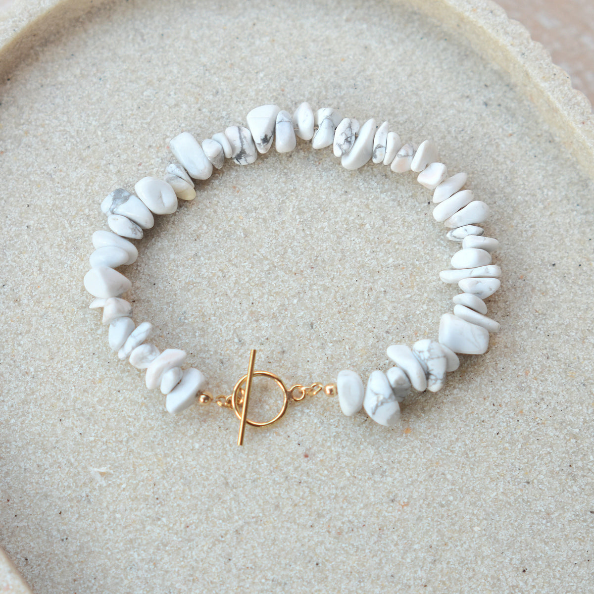 White turquoise bracelet with gold toggle on a beige tray